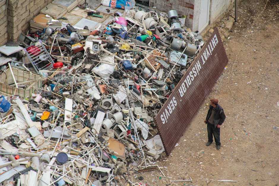 A waste collection truck operated by Mayfair Cleaners is parked on a city street, with the rear end raised and overflowing with large bags, cardboard boxes, and miscellaneous bulky waste. The truck fe